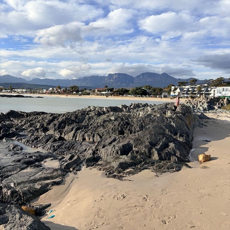 Rock formations on a sandy Cape coastline, with mountains across the bay.