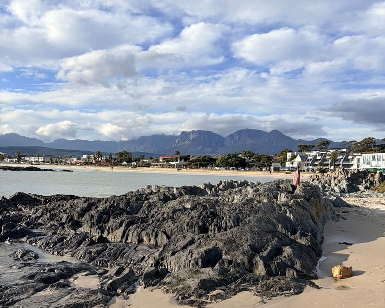 Rock formations on a sandy Cape coastline, with mountains across the bay.